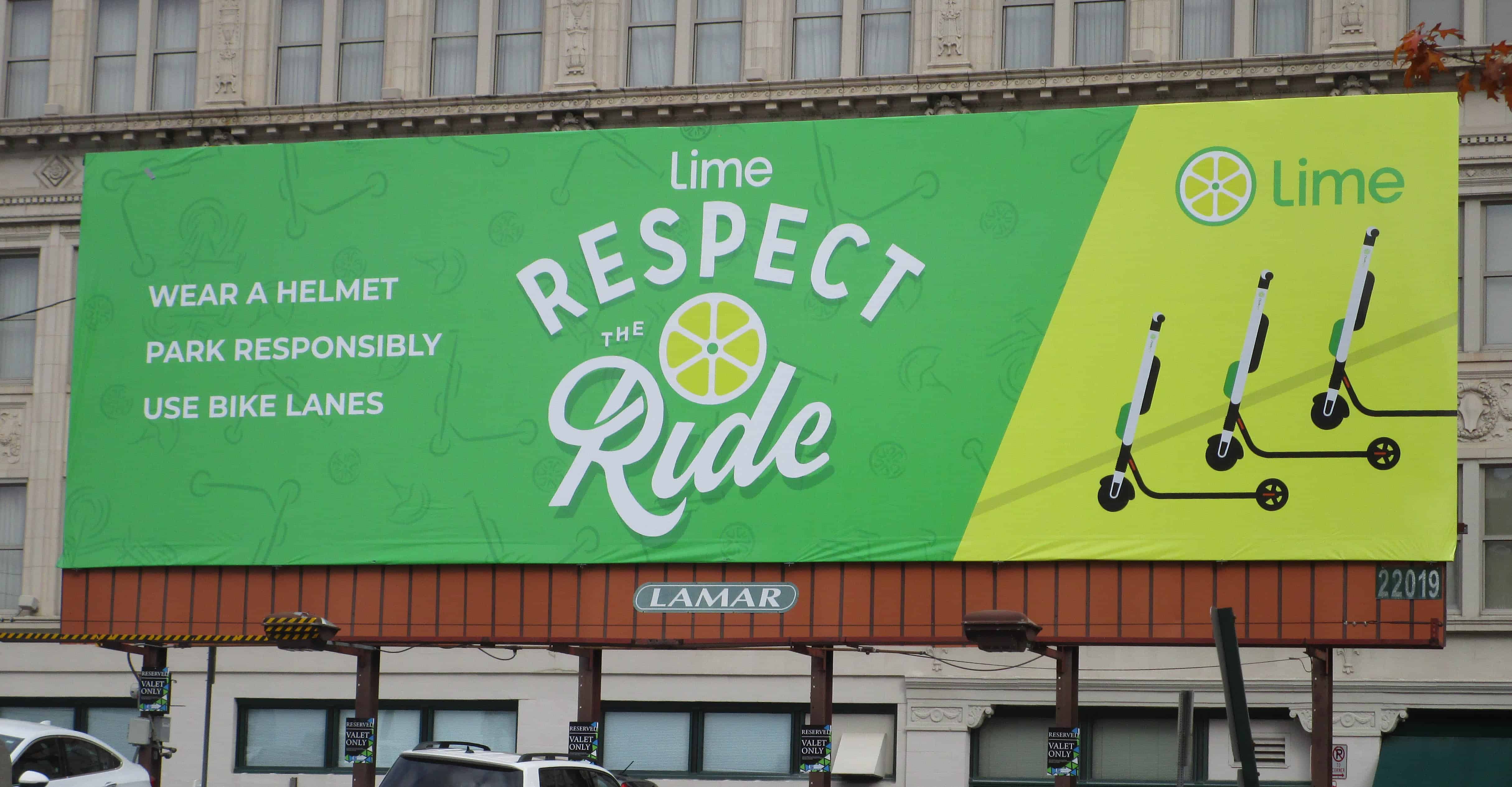 A large billboard with a green background displays Limes scooter safety message. It reads: Respect the Ride - Wear a Helmet, Park Responsibly, Use Bike Lanes. Three scooter icons are shown on the right side.