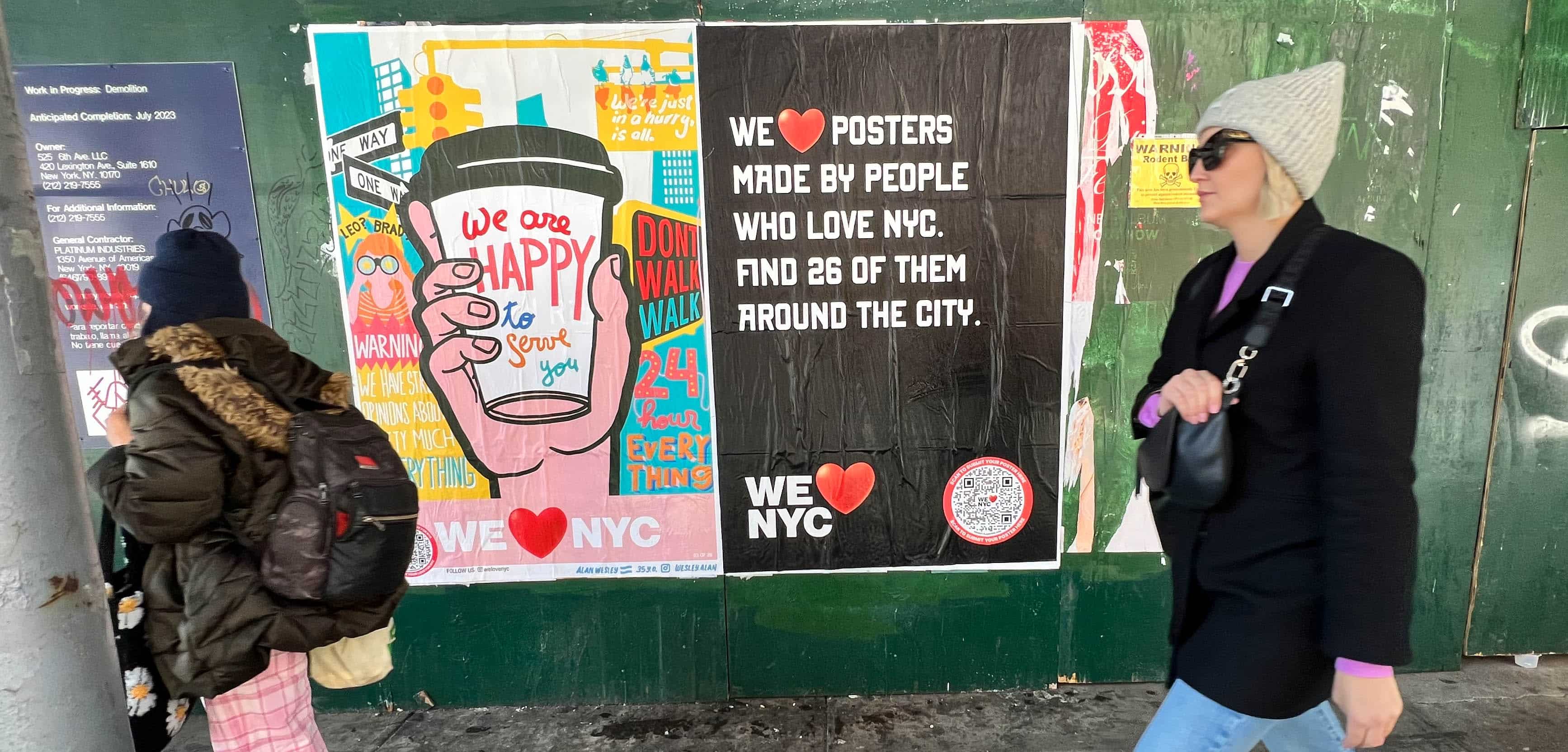 Two people walk past a green wall covered with colorful posters promoting NYC. One poster features a coffee cup with We ❤️ NYC and another promotes a poster campaign with 26 locations around the city. Both individuals are dressed warmly.