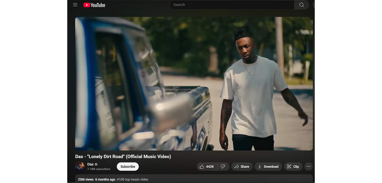 Dax in the “Lonely Dirt Road” official music video on YouTube, walking toward a vintage blue truck in a quiet suburban neighborhood.