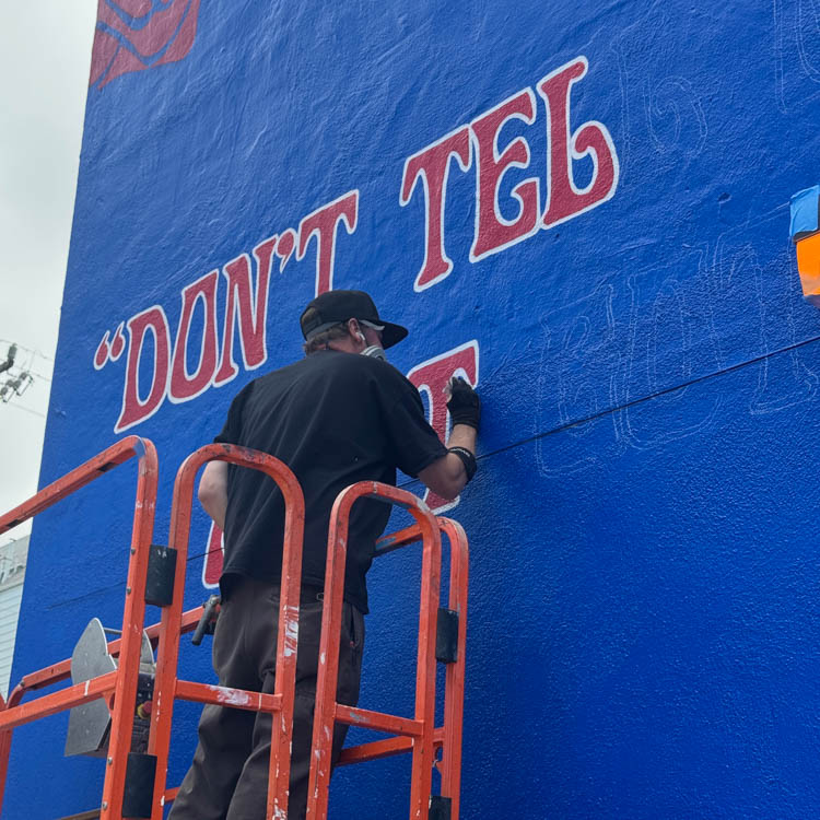 Artist painting Grateful Dead mural advertising on a blue wall