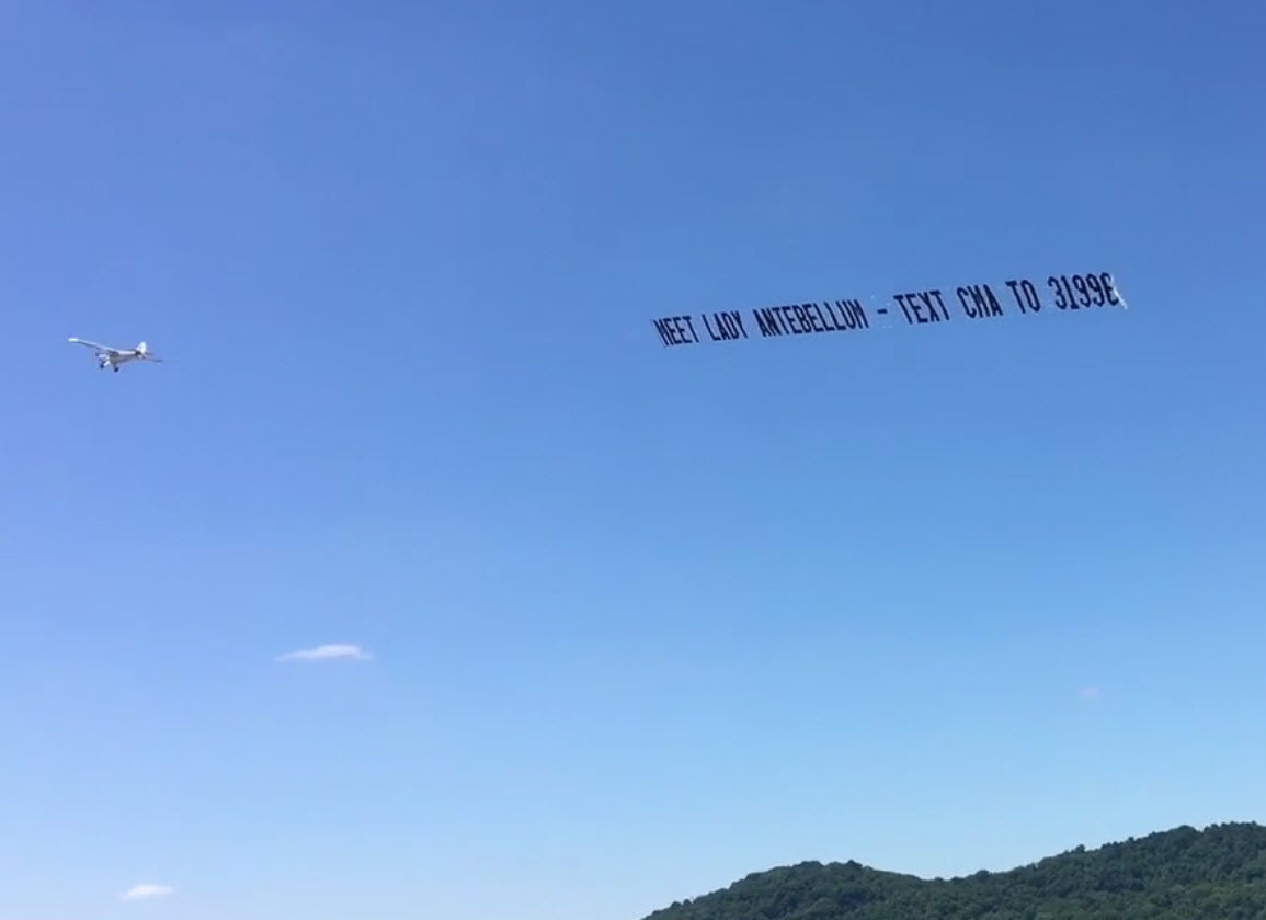 Airplane towing aerial banner advertising for Lady Antebellum CMA promotion over blue sky