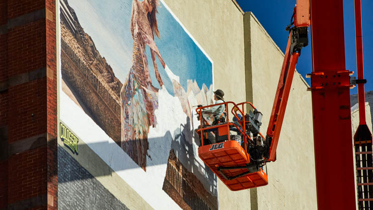 Mural artist painting a large-format wall mural on a lift