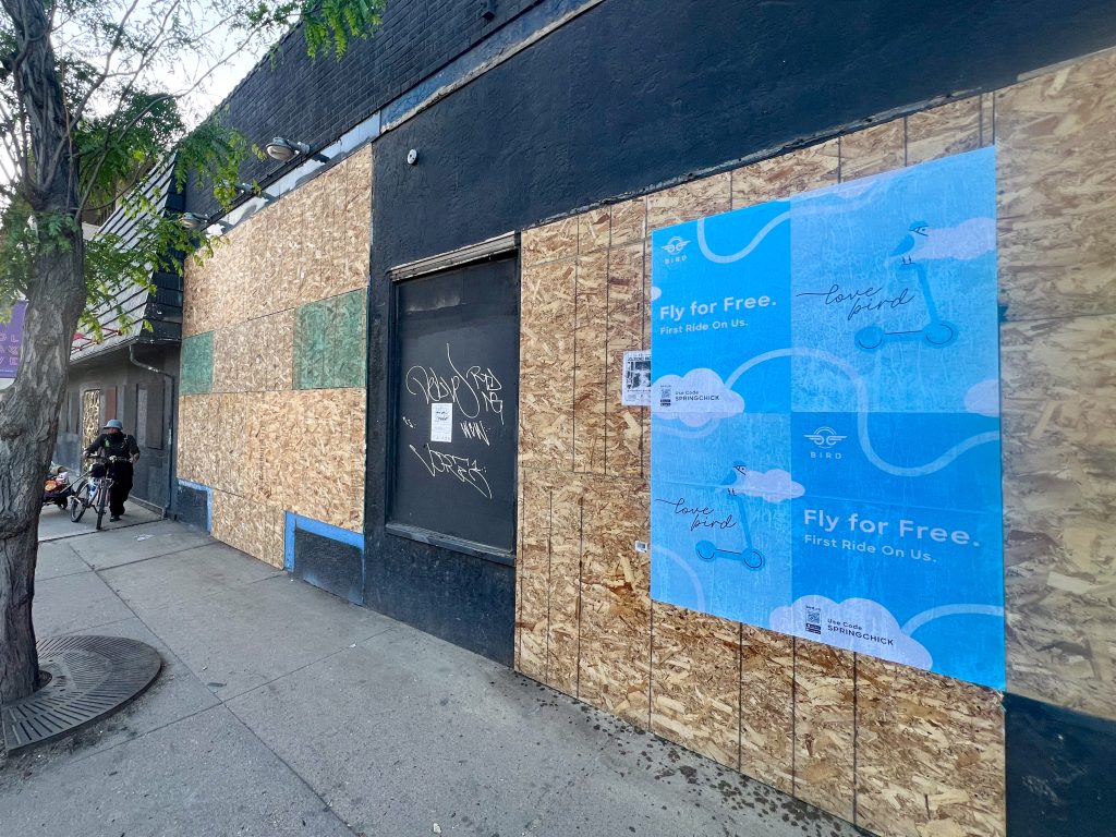Bird scooter wheatpasting posters on a boarded building in Denver