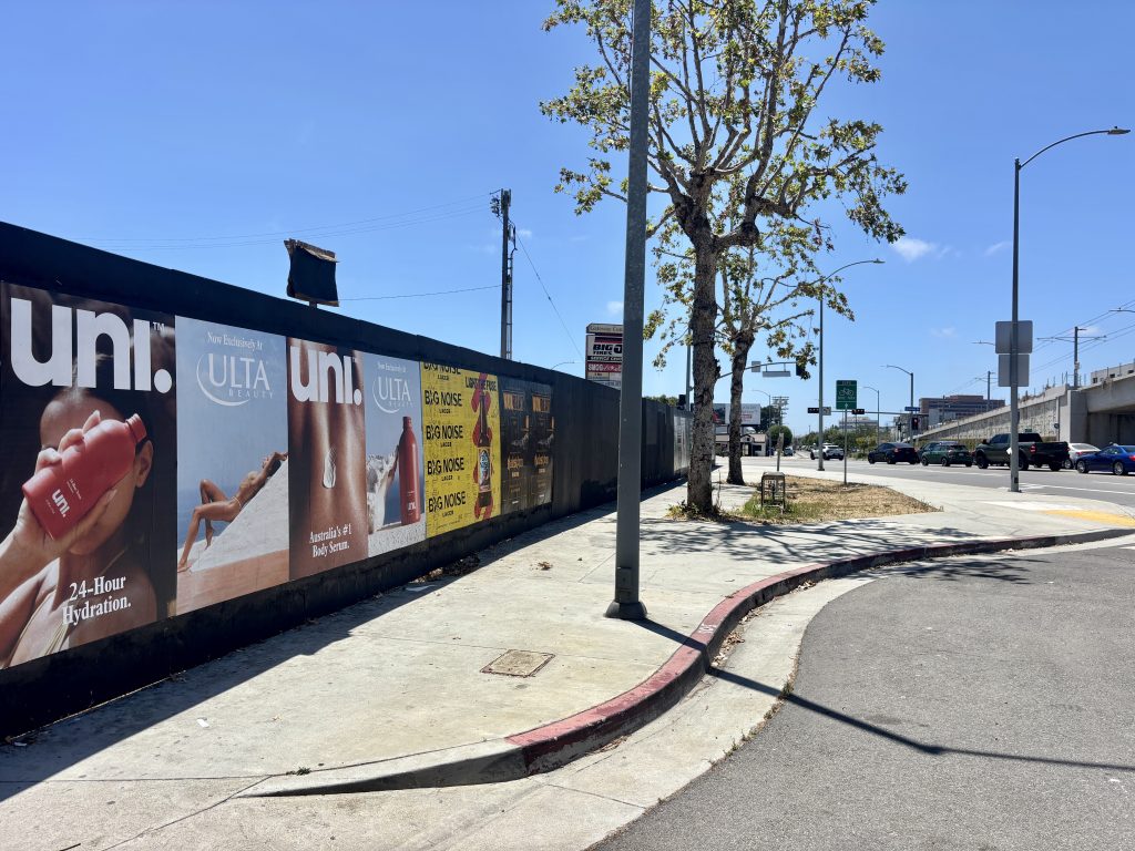 Multiple brand wheatpasting posters on a construction wall along Pico Boulevard in Los Angeles
