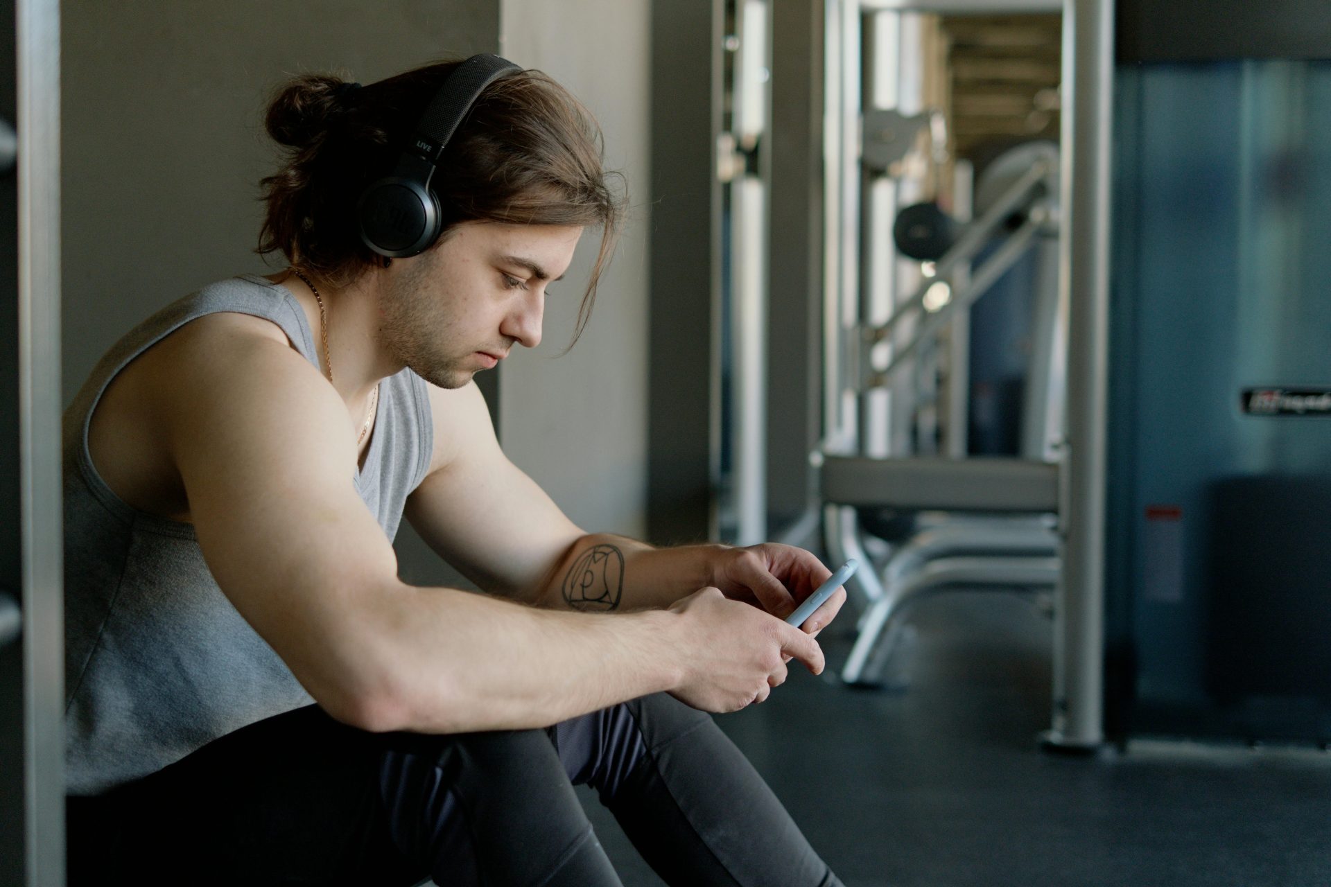 Man at gym wearing headphones listening to music on smartphone