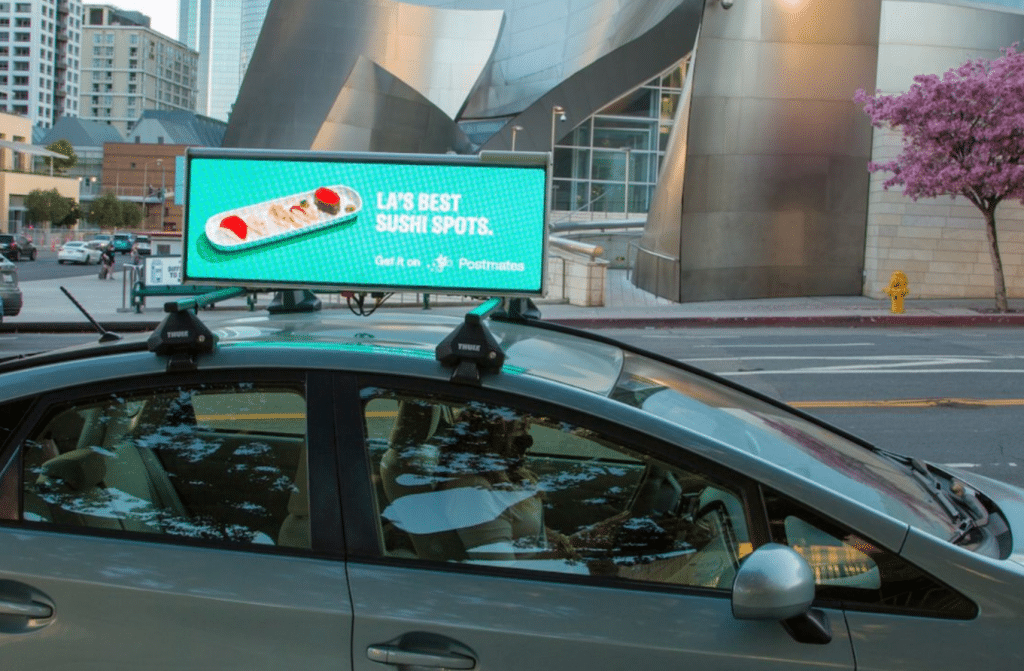 Postmates rooftop display ad on a rideshare vehicle in downtown Los Angeles