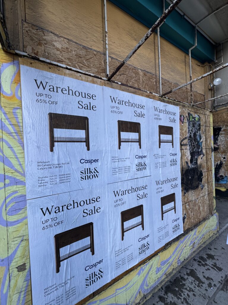 Poster advertising a Warehouse Sale with 'UP TO 65% OFF' and a chair image on a boarded wall surface.