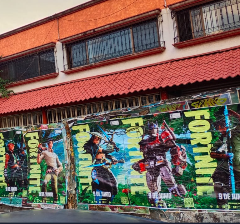 Colorful Fortnite poster wall advertising a game event beneath a red-tiled building canopy, featuring action figures and vibrant graphics.