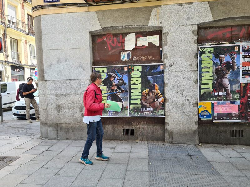Fortnite wheat pasting campaign on a Madrid street corner with pedestrian foot traffic — posters at eye level on a central Madrid building wall