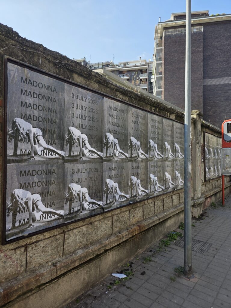 Madonna "Confessions II — 3 July 2026" Wheat Pasting and Wild Posting® wall takeover in Milan, with sixteen repeating panels on a permitted Comune di Milano affissione board.