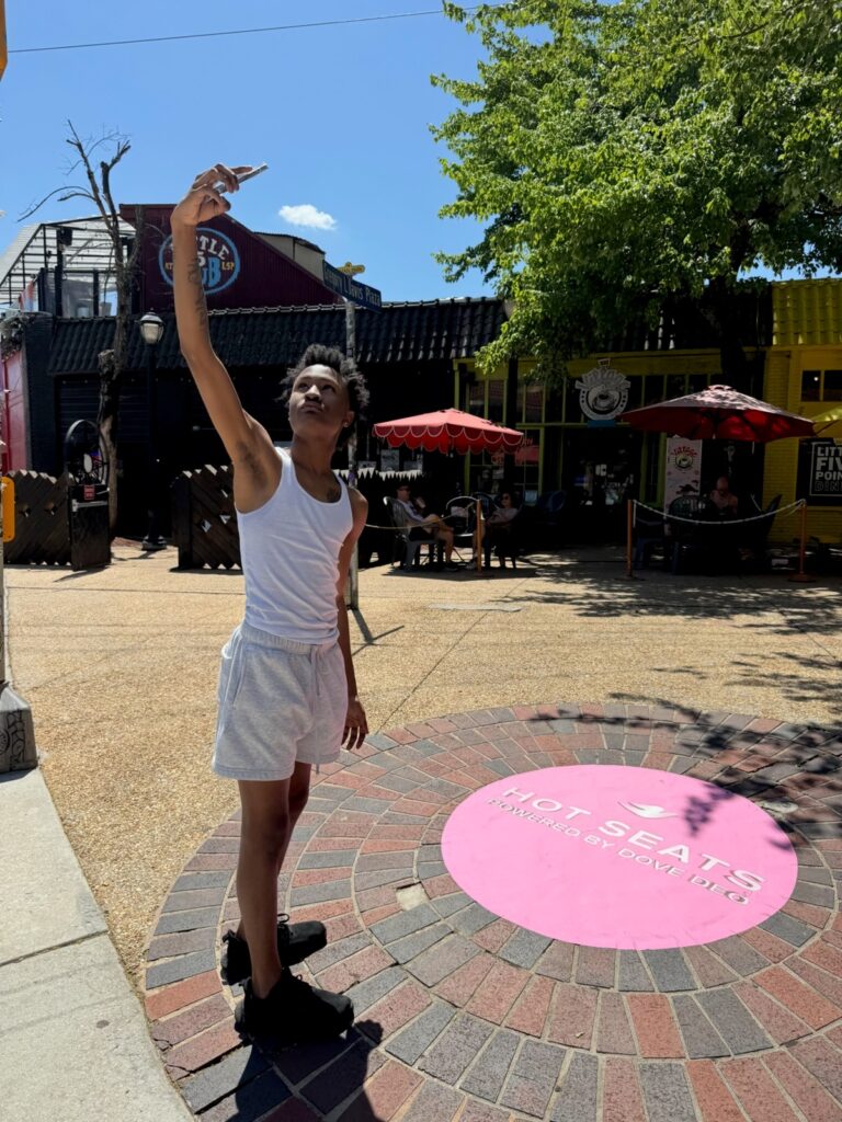 Young man taking a selfie next to a Dove deodorant Hot Seats pink sidewalk decal at Granny Lewis Plaza in Little Five Points Atlanta