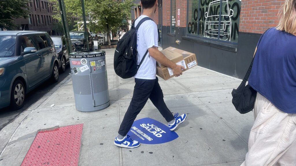 Just Salad blue die-cut sidewalk decal advertising campaign in Williamsburg Brooklyn with a pedestrian walking over it