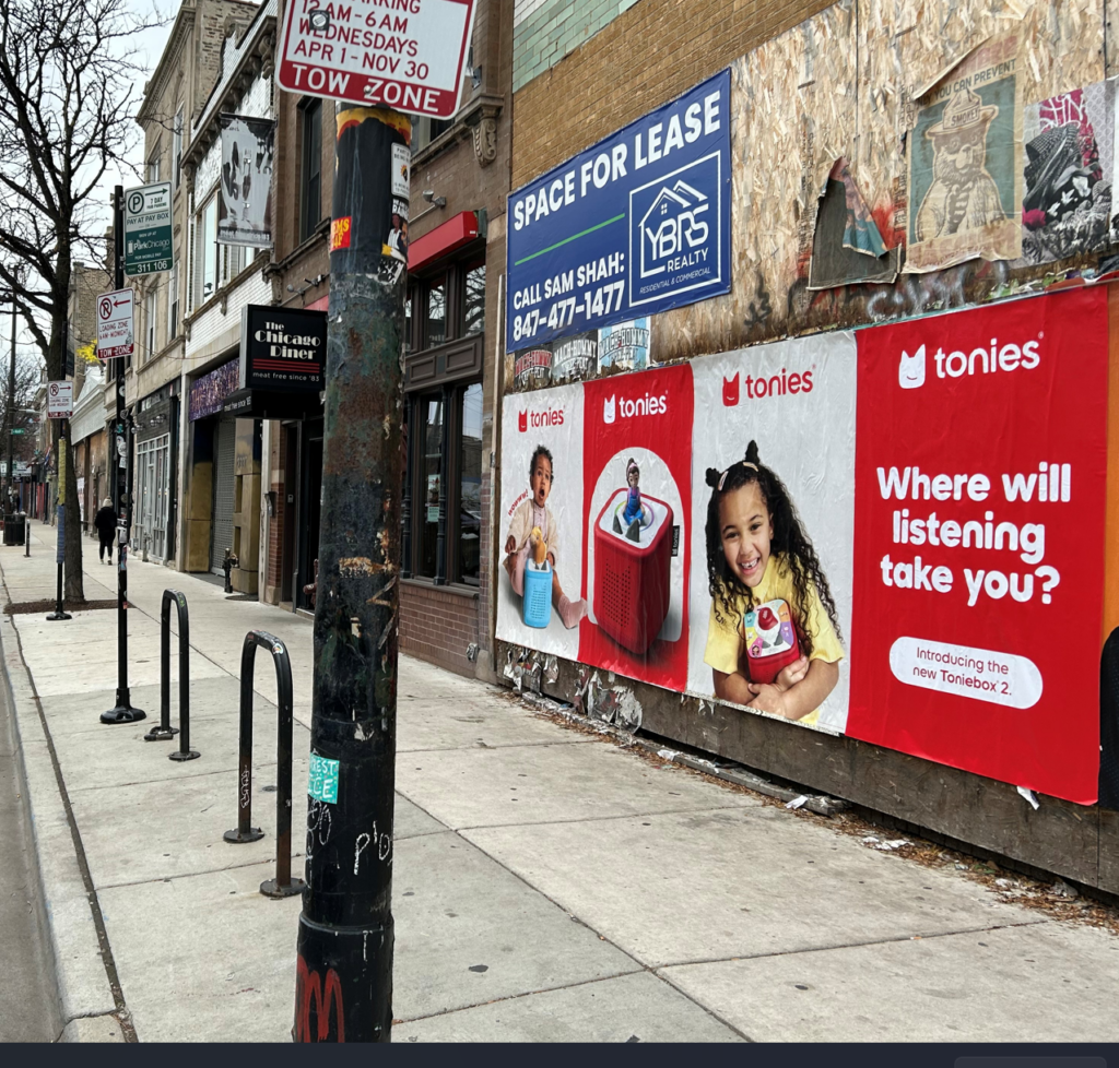 Tonies "Where will listening take you?" Wild Posting® campaign on a Milwaukee Avenue barricade wall in Chicago — wheat-pasted launch creative for the new Toniebox 2 children's audio player, placed across from The Chicago Diner.