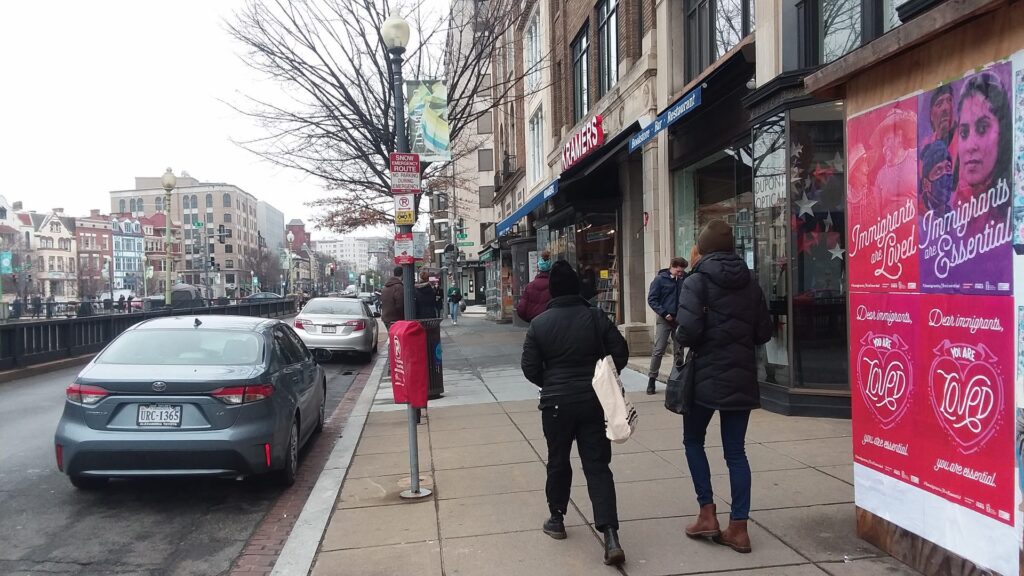 Wild Posting wheat pasting campaign on Connecticut Avenue near Q Street NW in Dupont Circle, Washington DC, with pedestrians walking past barricade posters outside Kramers bookstore.
