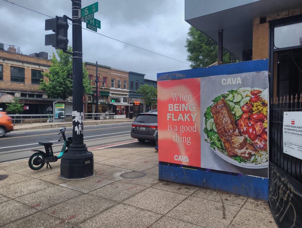 CAVA Wild Posting wheat pasting poster on 5th Street and H Street NE in Washington DC's Atlas District, with "When being flaky is a good thing" creative on a construction barricade.