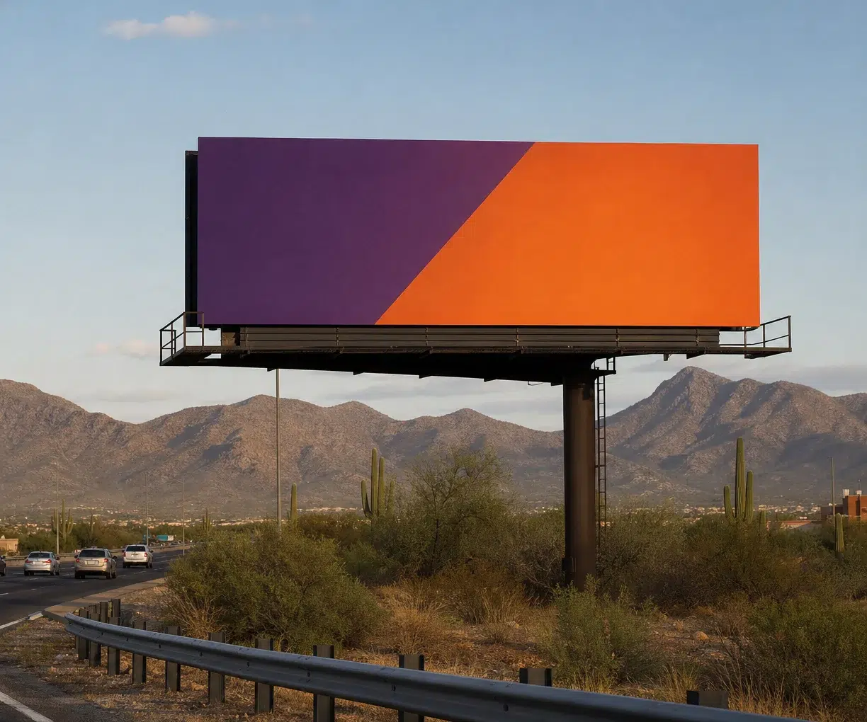Large rectangular billboard with purple and orange diagonal design mounted on a pole beside a desert highway.