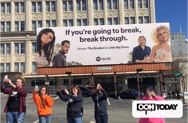 Group of people taking photos in front of a large city billboard that reads 'If you're going to break, break through' promoting Spotify.endash 'If you're going to break, break through' promoting Spotify.