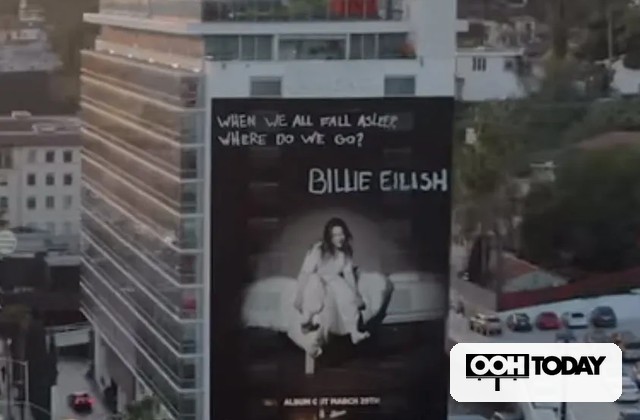 Billboard in a city showing Billie Eilish album cover, with the lyric 'When we all fall asleep, where do we go?' visible at the top and the OOH Today logo in the corner