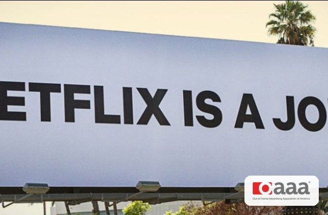 Billboard with bold black letters reading 'NETFLIX IS A JO...' in an outdoor setting, small aaa logo in the bottom-right corner and palm trees in the background.