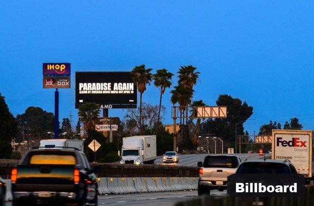 Busy highway at dusk with several cars and trucks; a large billboard reads 'PARADISE AGAIN' near palm trees.