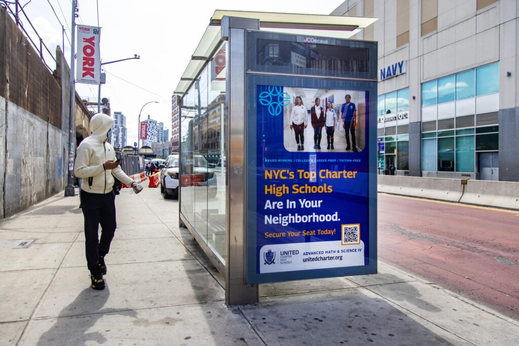 United Charter High Schools campaign on a JCDecaux bus shelter in Queens, New York, with a rider waiting at the shelter